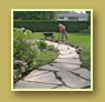 Flagstone walkway beside flowering shrubs and white gate.